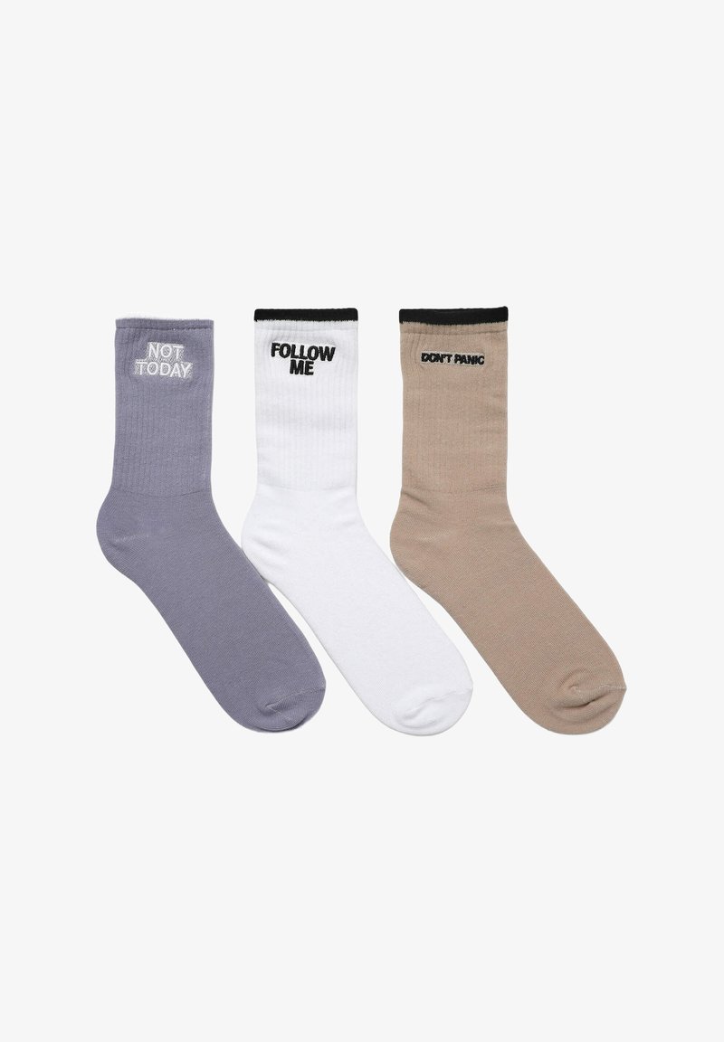 Trzy pary skarpetek w kolorze lawendowym, białym i beżowym, z kontrastującymi czarnymi ściągaczami. Każda skarpeta ma inny tekst: "NIE DZIŚ", "POPROWADŹ MNIE" oraz "NIE PANIKUJ".
