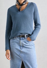 Pull bleu côtelé avec un col en V et des manches longues, associé à une jupe en jean claire avec une fente à l'avant et une ceinture noire.