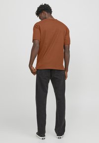 Camiseta marrón de manga corta hecha de algodón, con un corte relajado. Combinada con pantalones negros de pierna recta y zapatillas bajas.