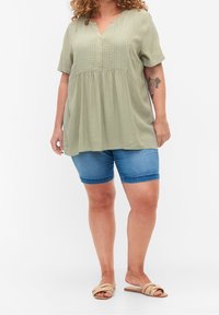 Olive green blouse with short sleeves, button front, and pleated design. Paired with denim shorts and beige slide sandals.