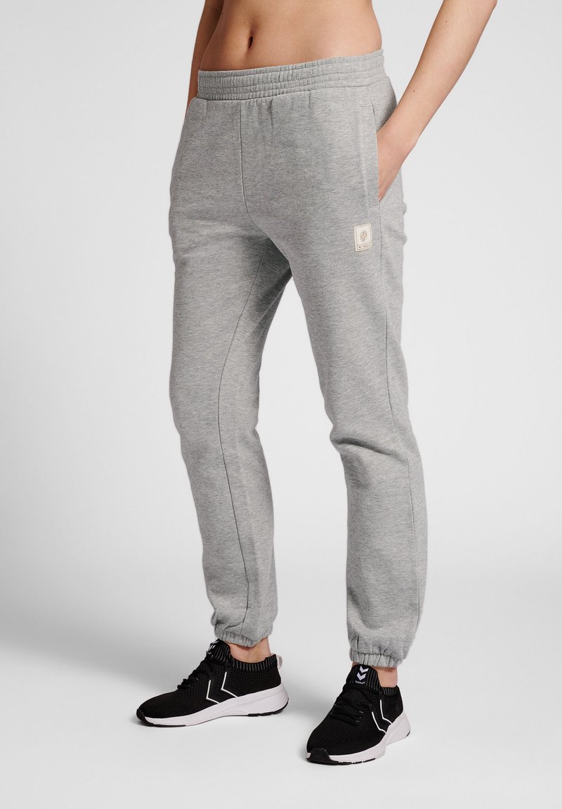 Grijze sweatpants met een elastische tailleband, zijzakken en een klein logo-patch op de dij. Gecombineerd met zwarte sportsneakers.