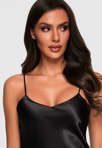 Camicetta in satin nera con sottili spalline regolabili, caratterizzata da una scollatura a V e una superficie liscia e lucida. Inquadratura ravvicinata della parte superiore del corpo.