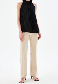 Svart plisserad halterneck-top i texturerad tyg, tillsammans med beige raka byxor. Öppen-toe svarta klacksandaler fulländar looken.