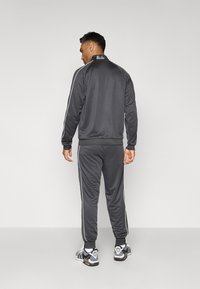 Gray tracksuit with white side stripes, featuring a zip-up collar and elastic cuffs, worn with patterned athletic shoes.