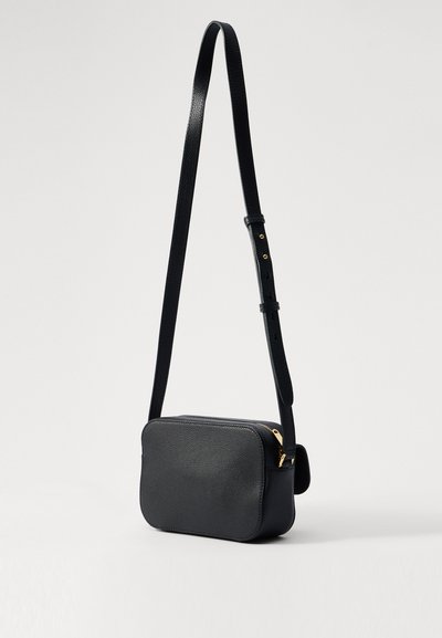 Svart läder crossoverväska med rektangulär form, guldfärgad dragkedja och justerbar rem. Texturerad yta och minimalistiska designelement.
