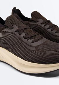 Sneakers nere traspiranti in maglia con motivi testurizzati ondulati, lacci neri e suole imbottite spesse di colore bianco sporco.