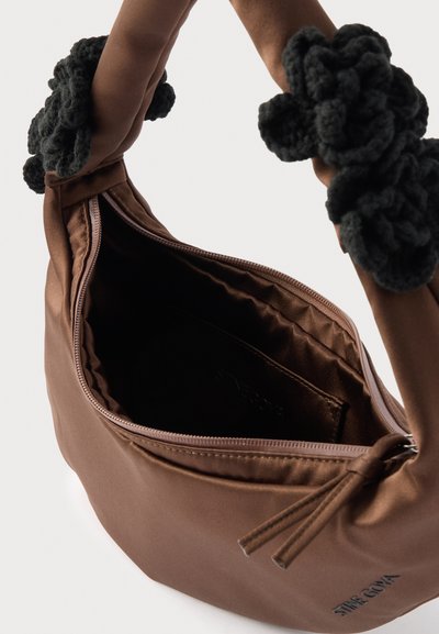 Καφέ υφασμάτινη τσάντα χειρός με μαύρα πλεκτά περιτυλίγματα στη λαβή, ανοιχτό φερμουάρ που αποκαλύπτει κενό εσωτερικό και μικρή εσωτερική τσέπη.