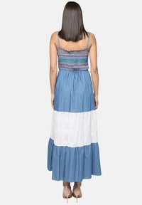 Vestido largo de mezclilla con corpiño bordado en azul y blanco. Presenta un diseño de capas con detalles de ojales y una parte inferior acampanada.