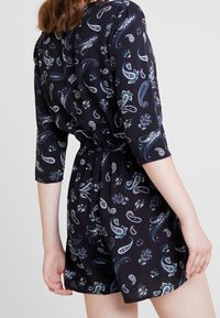 Mono negro con estampado de paisley, mangas tres cuartos, cintura ceñida y tejido fluido. Presenta acentos florales en azul y verde.