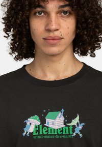 Schwarzes Baumwoll-T-Shirt mit einem bunten Grafikdesign, das verspielte Charaktere und ein Häuschen zeigt, mit grünen und blauen Akzenten.