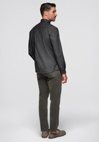 Chemise en denim foncé avec col, poignets à boutons et finition légèrement texturée, associée à un pantalon chino vert olive et des chaussures grises à enfiler.