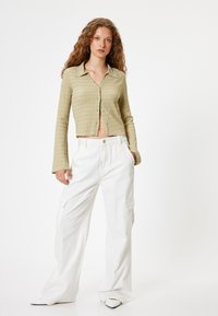 Chemise courte boutonnée texturée vert olive à manches longues, associée à un pantalon cargo large blanc avec des poches latérales et une taille ajustée.