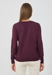 Burgunderfarbener Strickpullover mit langen Ärmeln und rundem Ausschnitt. Er zeichnet sich durch eine glatte Textur und einen gerippten Saum an den Bündchen und am unteren Ende aus.