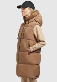Gilet marron rembourré avec un col montant et une capuche, doté d'une fermeture éclair frontale, de poches latérales et d'un subtil logo. Texture lisse et design simple.