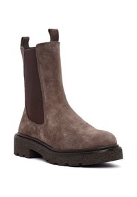 Botín Chelsea de ante marrón con paneles elásticos en los costados, punta redonda y suela texturizada. Cuenta con tiradores en el tobillo para ponerlo y quitarlo fácilmente.