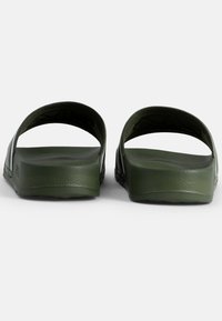 Gröna gummisandaler som är lätta att ta på sig, med en strukturerad yta, öppen baksida och böjda remmar. Släta invändigt med en subtil logotypdetalj på sidan.