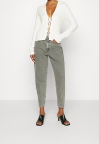 Modelo con top blanco de escote profundo en forma de V con detalle de cordones, combinado con unos jeans gris de cintura alta y tacones mule negros destalonados.