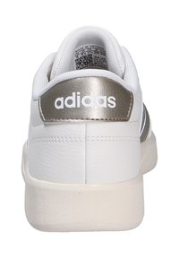 Vit sneaker med en strukturerad läderöverdel och metallisk silver hälla. Har "adidas"-logotypen i vitt och en gummisula.