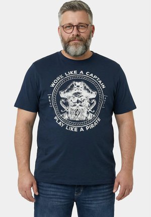 Uomo di mezza età con occhiali e barba che indossa una t-shirt blu navy con grafica di capitano pirata e testo "Lavora come un capitano, gioca come un pirata."