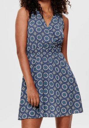 Mujer con vestido azul sin mangas con estampado de flores circulares y escote en V.