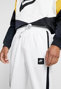 Vita idrottsbyxor med svarta sidostråk och en Nike Air-logga. Har en elastisk midja med dragsko för justerbarhet.