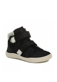 Botte montante noire en daim doux, dotée de deux sangles Velcro ajustables, d'une semelle en caoutchouc blanche et d'un détail de cheville gris texturé.