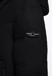 Czarna kurtka puchowa z kieszenią na zamek i metką z logo "FRIEDA FREDDIES" w białym kolorze na lewym rękawie.
