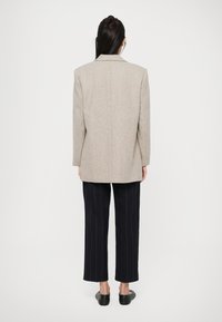 Beige wool-blend blazer with a structured design, notched lapels, and a single back vent, paired with dark pinstriped trousers.