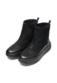 Botas de tobillo negras con parte superior de cuero liso y tejido texturizado. Presentan cremalleras en la parte delantera y una suela de goma gruesa y estampada.