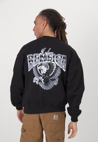 Black sweatshirt featuring a large eagle graphic and "S.L. BENFICA" text in white and grey, with a relaxed fit and ribbed cuffs.