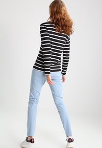 Mustat ja valkoiset raidalliset pitkähihainen paita yhdistettynä vaaleansinihin kapeisiin housuihin ja valkoisiin lenkkareihin, joissa on punaisia yksityiskohtia. Malli näkyy takaa.