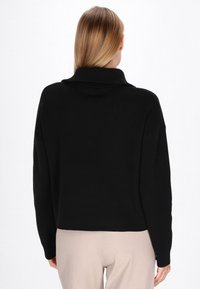 Maglione nero a collo alto con vestibilità morbida, texture a coste sul collo e sui polsini, dotato di maniche lunghe e lunghezza corta.