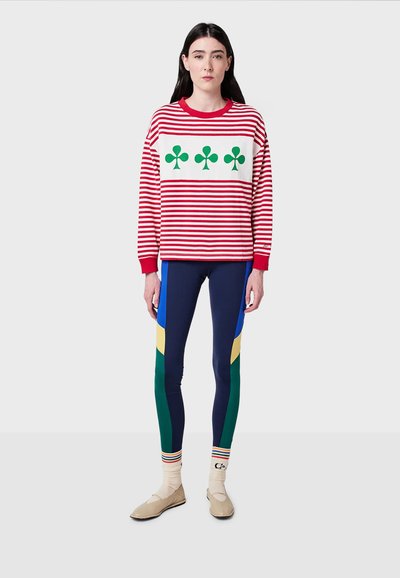 Felpa a righe rosse e bianche con un design di foglia verde; abbinata a leggings blu navy con accenti multicolori; scarpe beige e calzini a righe.