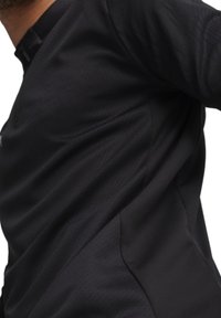 Zwarte sportieve longsleeve shirt met een gestructureerde stof en een halve ritssluiting. Heeft een getailleerd ontwerp en subtiele stiksels.