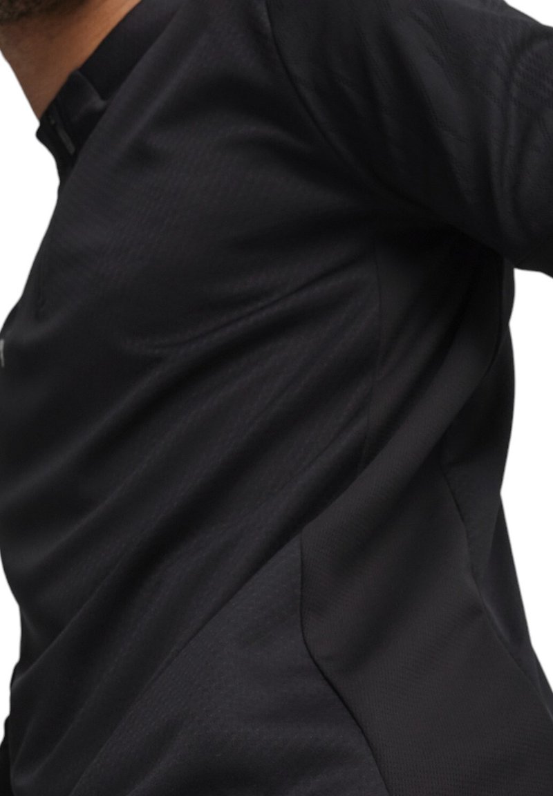 Zwarte sportieve longsleeve shirt met een gestructureerde stof en een halve ritssluiting. Heeft een getailleerd ontwerp en subtiele stiksels.