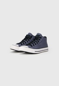 Sneakers altos feitos de lona azul-marinho com atacadores pretos, sola de borracha branca e bico texturizado. Apresenta riscas laterais contrastantes.