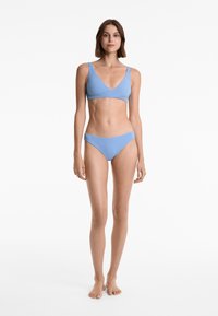 Svetlo modri bikini komplet, ki vključuje bralette zgornji del s širokimi naramnicami in V-izrezom, ter nizkocenovne bikini hlačke iz enakega materiala.