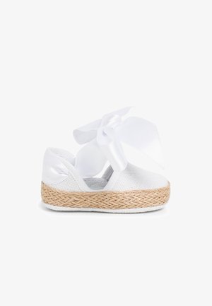 Witte espadrille schoen met een geweven stranden zool, bovenwerk van mesh en een grote witte strik geknoopt om de enkel. Gladde textuur overal.