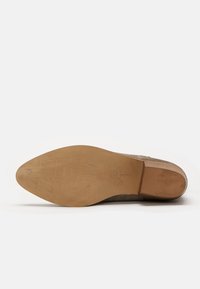 Scarpa in suede beige con punta affusolata, dotata di una suola in pelle liscia. La suola mostra dettagli incisi e un leggero tacco.