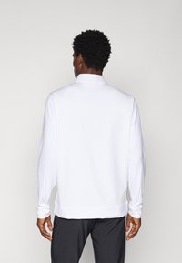 Biely dlhý rukáv pulóver s golierom, s hladkou textúrou a priliehavým strihom. Na zadnej strane sa nachádza jemný detail švu.