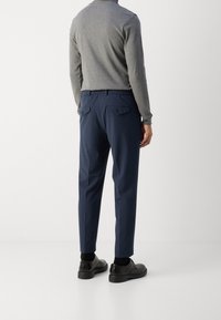 Granatowe spodnie o luźnym kroju, z elastycznym pasem i dwoma tylnymi kieszeniami. Noszone z szarą koszulą z długim rękawem i czarnymi butami.