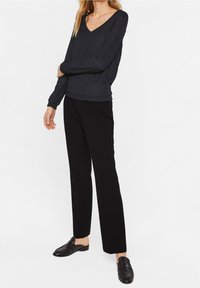 Mörkgrå ribbad långärmad topp med V-ringning, ihopparad med svarta raka byxor och svarta slip-on skor. Enkel design, avslappnad stil.