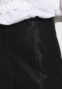 Musta nahkahame, jossa on teksturoitu pinta ja sivulla piilotettu vetoketj yksityiskohta. Yhdistetty valkoiseen yläosaan, jossa on reikäkoristeita.