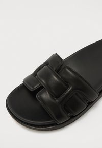 Must kukkade sandaalid mustast nahast, millel on kaks laiade, polsterdatud rihma, sile pind ja lame tallaosa, millel on kerge tekstuur.