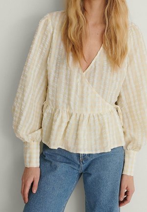 Gul- og hvidternet slå-om-bluse med lange pufærmer og en flæsekant, lavet af let stof. Kombination med blå jeans.