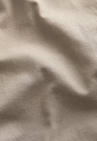 Bežani teksturirani materijal s mekim, tkanim izgledom, koji prikazuje suptilne nabore i pregibe. Čini se da je materijal izdržljiv i lagan.