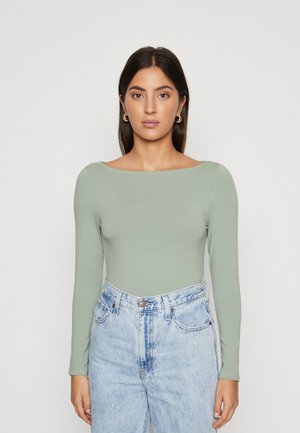 Pikkaels õlgadega bodi helesinisest pehmest ja venivast kangast, millel on paadi kaelus. Kombineeritud kõrge vöökohaga sinistest denim jeansidest.
