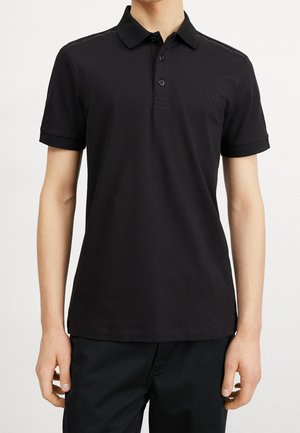 Man draagt een effen zwart poloshirt met korte mouwen, kraag en twee knopen, gecombineerd met een zwarte broek.