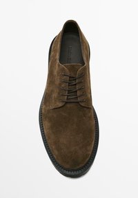 Chaussure en cuir suédé brun à lacets avec un embout rond et une semelle en caoutchouc noir. Présente cinq œillets et une texture lisse. Branding minimal visible.