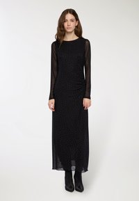 Czarna sukienka z długim rękawem z przezroczystą nakładk�ą, z małymi srebrnymi kropeczkami i marszczonym detalem z boku. Stylizowana z czarnymi botkami za kostkę.